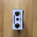 Fotografie zachycuje zadní stranu bílého efekt pedálu značky tc electronic. Jsou zde vidět dva jack konektory s nápisy INPUT a OUTPUT a středový napá…