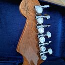 Záběr na zadní stranu hmatníku elektrické kytary z hnědého dřeva s viditnou masivním kresbou. Na dřevě je nápis "Custom Shop" a logo "Fender". Na pra…