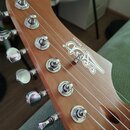 Detail hlavy elektrické kytary z hnědého dřeva s pěti ladicími kolíky. Na povrchu je bílý nápis JET GUITARS a stylizované logo v podobě písmen. Povrc…