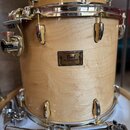 Světle hnědý buben s přirozenou dřevěnou strukturou a chromovaným kováním. Uprostřed korpusu je černé štítkové logo s nápisy Pearl, Masters Custom a…