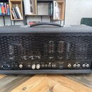 Černý kytarový kombozesilovač s texturovaným povrchem a kovovými rohy. Zadní panel obsahuje ovládací prvky a nápisy: POWER, FUSE TAP, FUSE MAIN, RECT…