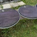 Tři kulaté bubnové membrány s bílým okrajem položené na kusu dřeva v trávě. Membrány jsou tmavě fialové až černé barvy s viditelnou texturou. Každá z…