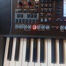 Detailní pohled na ovládací panel a klávesy elektronického klavíru v černé barvě. Panel obsahuje různé tlačítka, posuvníky a dva otočné knoflíky s ná…