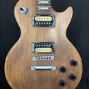 Elektrická kytara s hnědým dřevěným povrchem a dvěma humbuckery. Na přepínači je nápis TREBLE. Kytara má čtyři černé oválné knofíky a stříbrný most s…