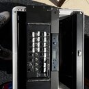 Černý digitální mixážní pult značky Behringer, model X AIR, osazený v hliníkovém transportním kufru. Na zadním panelu jsou vidět různé vstupy a výstu…
