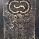 Detail zadní strany černého kytarového cabinetu s přišroubovaným dřevěným štítkem. Na štítku je vyryto logo ve tvaru stylizovanýchvln a nápis COFFE C…