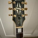 Detail hlavy elektrické kytary v černé barvě se zlatým lemováním. V horní části je bílý nápis Orville a na krytce trstrnu nápisy Les Paul CUSTOM. Na…