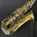 Zlatý saxofon s kovovým povrchem. Na zvonu je viditelný nápis YAMAHA. Nástroj vykazuje známky používání v podobě drobných škrábanců a otěrů na laku.