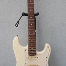 Bílá elektrická kytara typu Stratocaster s hnědým hmatníkem a krčkem z přírodního dřeva. Na hlavě je svisle umístěné logo "LAVA MUSIC". Kytara má tři…
