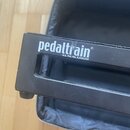 Černý kovový pedalboard s nápisem pedaltrain® a textem U.S. Pat. No. 6,459,023. Povrch rámu vykazuje drobné škrábance a prach. Pod nástrojem je vidět…