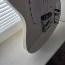Detail spodní části těla bílé elektrické kytary s bílým pickguardem. Na nástroji jsou vidět dva ovládací knofíky, přepínač tónů a kobylka s pružinami…