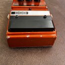 Oranžový efekt pedál s třemi černými oválnými knoflíky. Na horní části je nápis CLASSIC FUZZ a označení FX52, v bílém poli je logo DOD. Zařízení vyka…