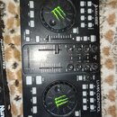 Černý DJ kontrolér s nápisy MIXVIBES a U-MIX CONTROL. Zařízení obsahuje dva jog-kola s výrazným zeleným logem Monster Energy, posuvníky a několik ovl…