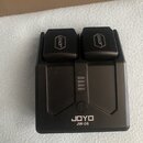 Černá nabíječka na baterie s dvěma sloty. Na horních krytech je logo JOYO a v dolní části nápis JOYO JW-06. Uprostřed se nachází kontrolka s čtyřmi s…