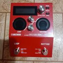Červený loop pedal značky BOSS s nápisem LOOP STATION RC-10R. Zařízení má digitální displej, dva velké černé ovladače a dva menší kovové knoflíky s p…