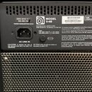 Detail zadní strany přístroje s černým povrchem a kovovou mřížkou v dolní části. Na štítku jsou uvedeny údaje 220-240 V~ 50-60 Hz, POWER CONSUMPTION…
