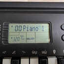 Detail ovládacího panelu černého digitálního klavíru s LCD displejem. Na displeji je zobrazen nápis 00 Piano 1 a hodnota 120 u ikony metronomu s nápi…