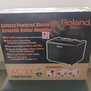 Fotografie znázorňuje kartónovou krabici s produktem Roland Battery Powered Stereo Acoustic Guitar Amplifier. Na krabici je uveden model AC-33 ACOUST…