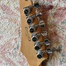 Detail hlavy kytary z přírodního dřeva s šesti chromovanými ladicími kolíky. Na každém kolíku je černý kryt s nápisy LOCKING LOCK, GOTOH MADE IN JAPA…