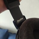 Detailní pohled na černý plastový rám sluchátek s hnědým polstrováním. Na rámu je bílý nápis Massdrop a v horní části je vyražen text MADE IN IRELAND…