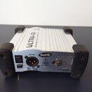 Stříbrná DI box s černými gumovými nárožníky. Na horní části je nápis ULTRA-DI a text ACTIVE DIRECT INJECT BOX FOR MUSIC STUDIO. Zadní panel obsahuje…