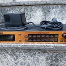 Kytarový efektový procesor v oranžovém provedení s nápisem GUITAR EFFECTS PROCESSOR. Na horní části jsou tlačítka v sekci EFFECT SELECT s označením P…
