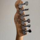 Zadní strana dřevěné hlavy basové kytary s pěti chromovanými ladicími mechanismy. Na dřevě je černý nápis Designed and Backed by Fender s číslem s/n…