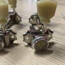 Detailní pohled na čtyři chromované ladicí mechanismy s krémovými plastovými knoflíky. Na kovových krytech je vyryt nápis GOTOH a logo ve tvaru styli…