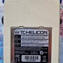 Zadní strana bílého efekt pedálu značky TC HELICON. Na kovovém štítku je uveden text: „FOOT SWITCH HOLD TONE DURING POWER-UP TO ENTER AND EXIT MOMENT…
