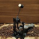 Černý bicí pedál s kovovou konstrukcí a stříbrným šlapadlem. Mechanismus pohonu je řešen řetězem. Na pedálu nejsou viditelné žádné značky ani nápisy.…