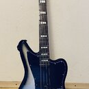 Elektrická basová kytara s offsetovým tvarem korpusu v černo-stříbrném přechodovém lakování. Na hlavě hmatníku je bílý nápis Squier JAGUAR BASS. Nást…
