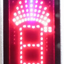 Detailní záběr na červený LED displej ladícího zařízení. Displej zobrazuje svítící symbol připomínající stylizovanou budovu s paprčitým vrchem. V dol…
