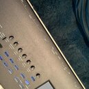 Detailní pohled na ovládací panel šedého elektronického klávesového nástroje. Jsou vidět různé ovládací knofíky s popisky jako CUTOFF GATE, RESONANCE…