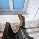 Fotografie zachycuje detail zadní strany těla elektrické kytary s černým povrchem a dřevěnými hranami. Na těle je bílý nápis v kurzívě, ze kterého js…