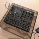 Černý digitální sampler a sekvencér s nápisem Digitakt a logem Elektron. Zařízení má malý displej, několik otočných knoflíků a mřížku 16 šedých podsv…