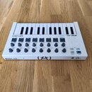 Bílá MIDI klaviatura s 25 klávesami umístěná na dřevěné podlaze. Na přístroji jsou nápisy ARTURIA, MINILAB a logo (A). Ovládací panel obsahuje osmtoč…