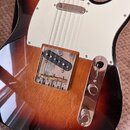 Detail elektrické kytary s tónem sunburst a bílým pickguardem. Nástroj má jeden snímač s chromovaným krytem a chromovaný most s šesti saddles. Na chr…