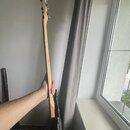 Fotografie zachycuje elektrickou kytaru v černé barvě, kterou drží ruka. Je vidět hmatník a hlava kytary zC světlého dřeva s kovovými ladičkami. Na n…