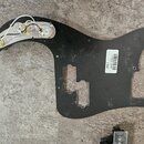 Černý plastový pickguard do elektrické kytary s instalovaným potenciometrem a přepínačem. Na povrchu je bílá papírová nálepka s čárovým kódem a nápis…