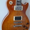 Elektrická kytara typu Les Paul s hnědým slunečním odstínem (sunburst) a viditnou strukturou dřeva. Nástroj má dva humbuckery s krémovými rámečky, čt…