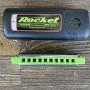 Černý plastový přístroj s nápisem Rocket amp, pod kterým je uveden text PROGRESSIVE, Matthias Hohner a Made in Germany. Na pravé straně je vyryto log…