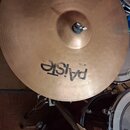 Zlatavý činel s viditelným obrubováním povrchu. Na spodní části je černý nápis Paiste a menší kód 20 318E. Činel je upevněn na stojanu pomocí šroubu…
