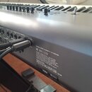 Detailní pohled na zadní panel stříbrného klávesového nástroje s připojenými kabely. Na šasi je vidět nápis California 93120 compliant for formaldehy…