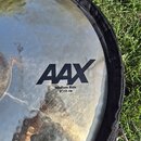 Detailní záběr na kovový činel v černém textilním obalu. Na povrchu je černý nápis AAX a pod ním text Medium Ride 21"/53 cm. Povrch činelu vykazuje d…