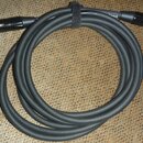 Svinutý šedý audio kabel s konektory XLR na obou koncích. Kabel je stahován černým suchým stahovadlem, na kterém je vidět část nápisu "nd". Povrch ka…