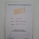 Bílý papírový certifikát s nápisem CERITIFICATE OF AUTHENTICITY a zlatým logem Henry's. Ručně jsou v něm vyplněna pole Date 24.5.24, Model HEC3MSTSN3…