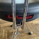 Černý polstrovaný sedák bubeníckého trůnu s červeným prošíváním. Na boku je umístěn štítek s červeným nápisem Pearl Roadster THRONE. Podsedák je upev…
