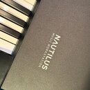 Detailní pohled na část klávesového nástroje s černým, jemně strukturovaným povrchem. Na šasi je bílý nápis NAUTILUS a pod ním menší text MUSIC WORKS…