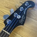 Detail hlavy černé basové kytary s nápisy Squier by Fender a JAGUAR BASS. Na hlave jsou čtyři chromované ladičky a stříbrný trstrnový matice. Povrch…