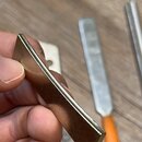Detailní pohled na kovový, zlatavý nástavek nebo díl s obdélníkovým tvarem. Povrch vykazuje drobné škrábance a známky opotřebení, zejména na hranách.…